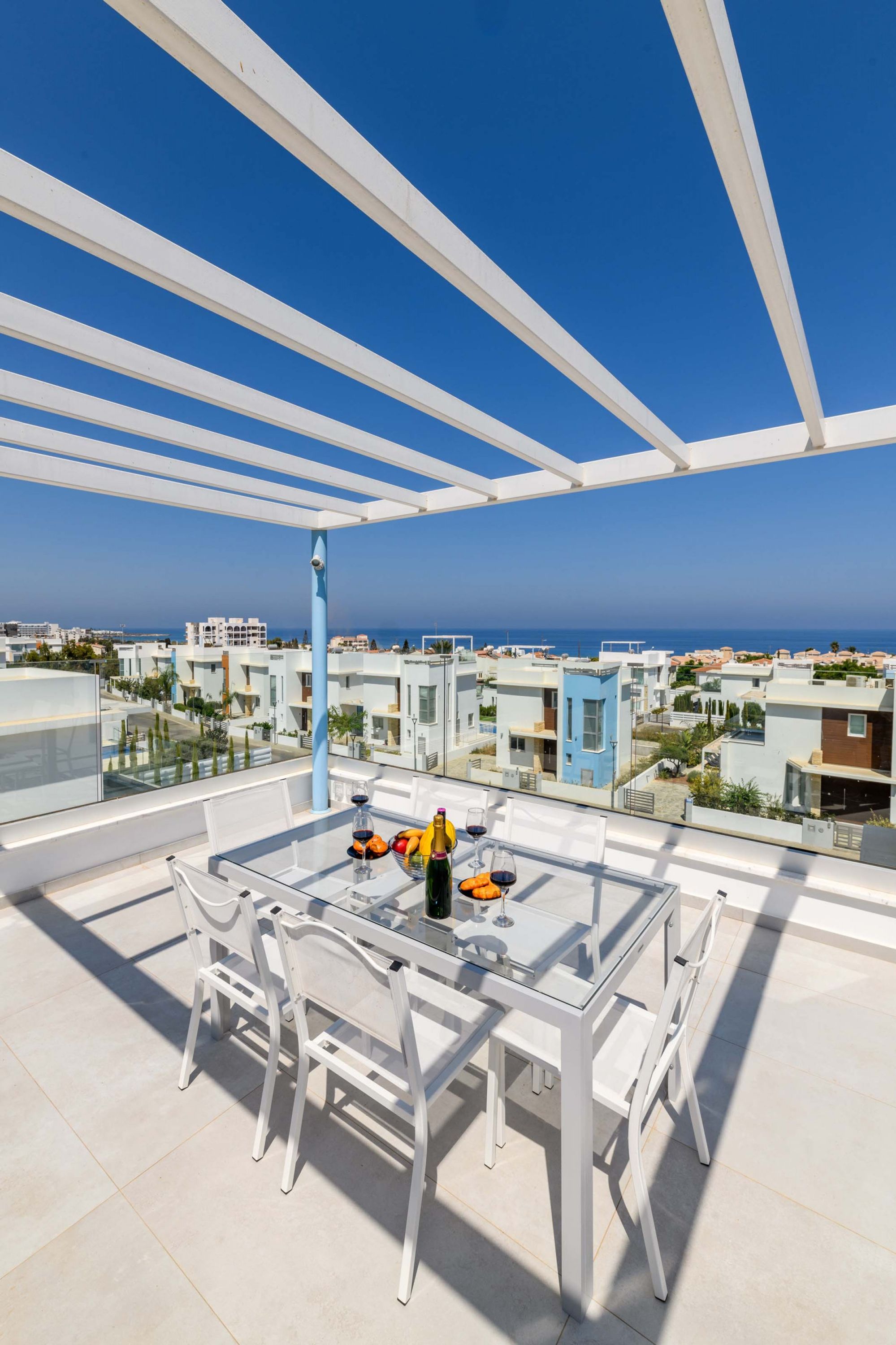 Une terrasse extérieure moderne, dotée d’une table en verre et de chaises blanches, qui offre une vue sur le paysage urbain de la côte.