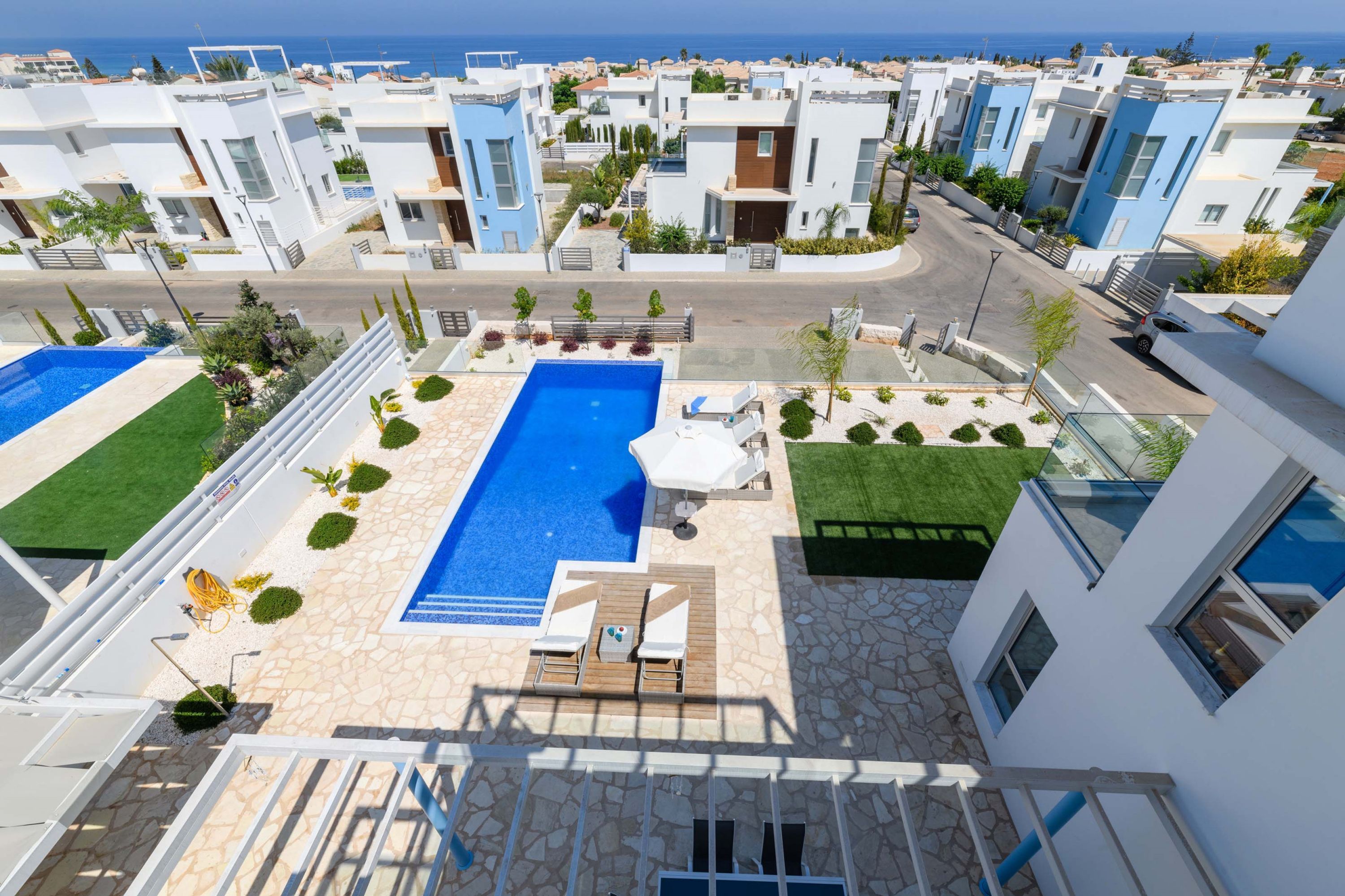 A modern residential area with a central swimming pool, surrounded by well-maintained lawns and a few trees.