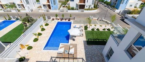 A modern residential area with a central swimming pool, surrounded by well-maintained lawns and a few trees.