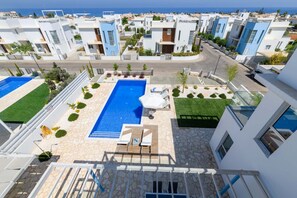 Una zona residencial moderna con una piscina central, rodeada de céspedes cuidados y algunos árboles.