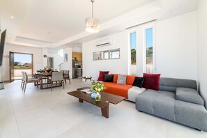 A modern living room with a grey sofa, a wooden coffee table, and a dining area with a table and chairs. - Mylos Lifestyle Seaview Villa 21 (Paralimni)