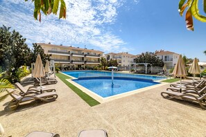 A pool area with lounge chairs and umbrellas, surrounded by buildings. - Mythical Sands Ae01 in Protaras (Paralimni)