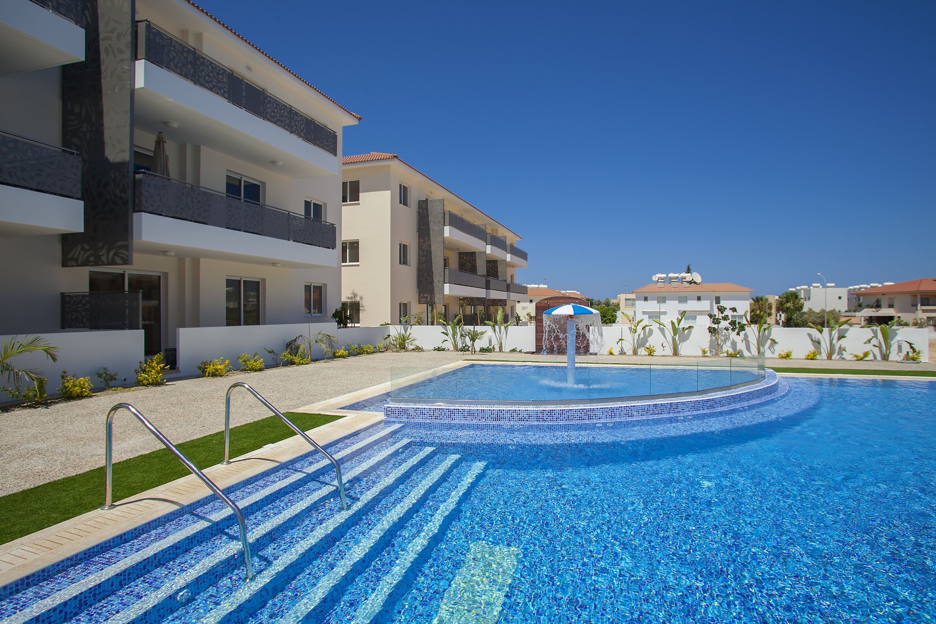 A modern hotel with a swimming pool, multiple balconies, and a clear blue sky.