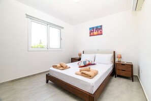 A bedroom with a bed, two nightstands, a window, and a painting on the wall. - Mythical Sands Ae01 in Protaras (Paralimni)