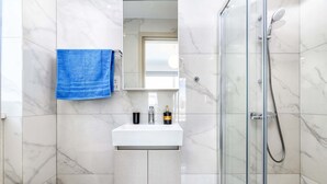 Uma casa de banho com uma pia branca, uma toalha azul e um chuveiro com parede de vidro.