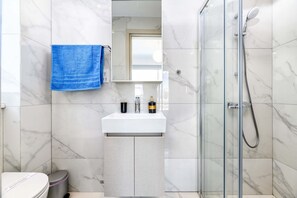Un baño con un lavamanos blanco, una toalla azul y una ducha con cerramiento de vidrio.