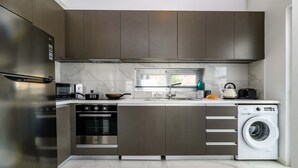 A modern kitchen with stainless steel appliances, a built-in oven, a microwave, and a washing machine.