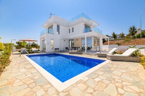 Una casa moderna de dos pisos con piscina, mobiliario exterior y un patio cubierto.