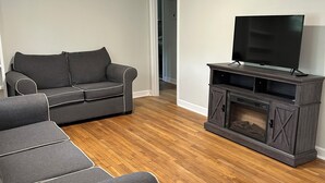 A living room with a grey sectional sofa, a flat-screen TV on a wooden entertainment unit, and hardwood flooring. - 3-bedroom house in marvelous Athens (Athens)