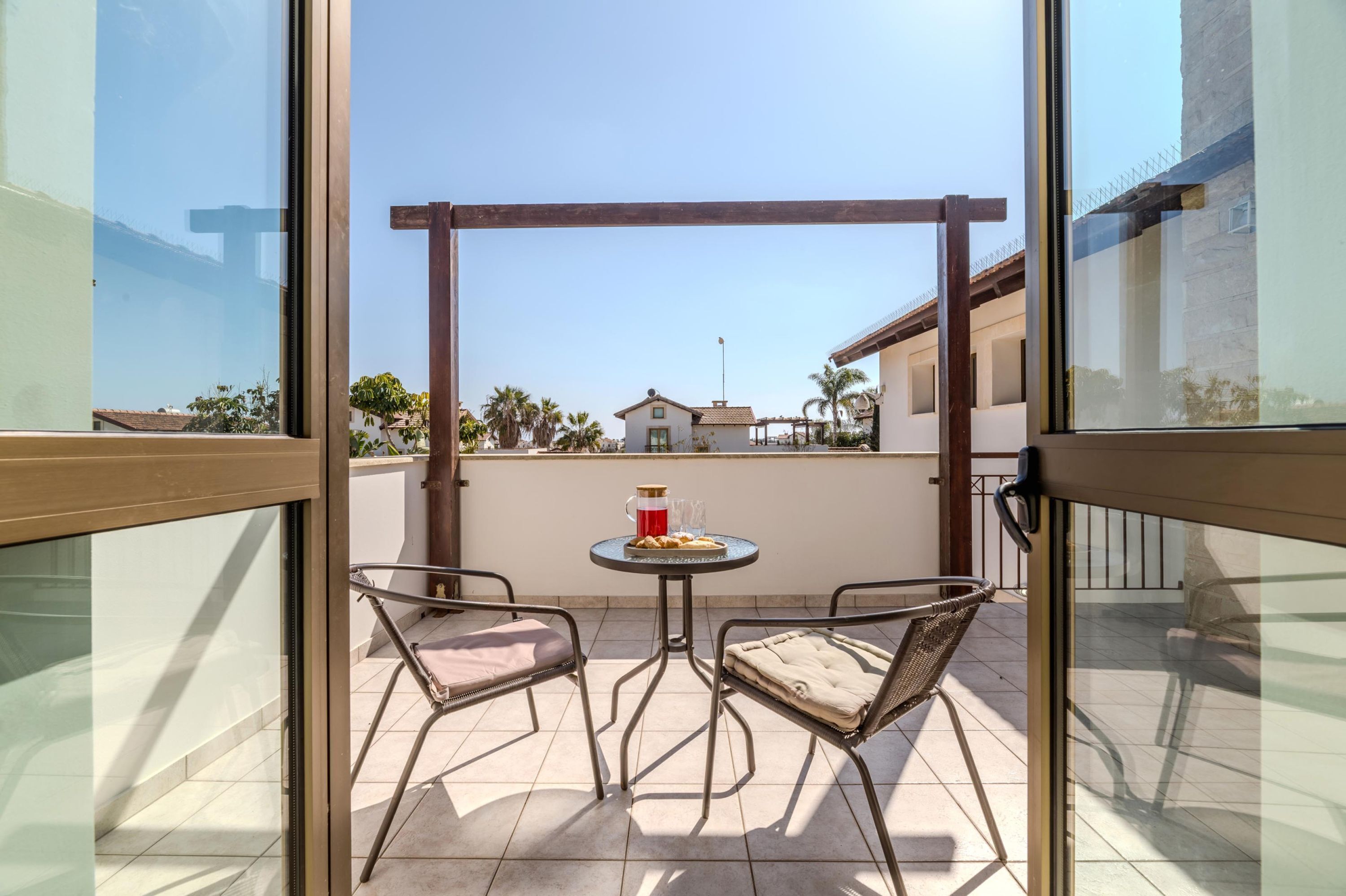 A balcony with two chairs and a small table, a clear view of the neighborhood, and a building in the background.