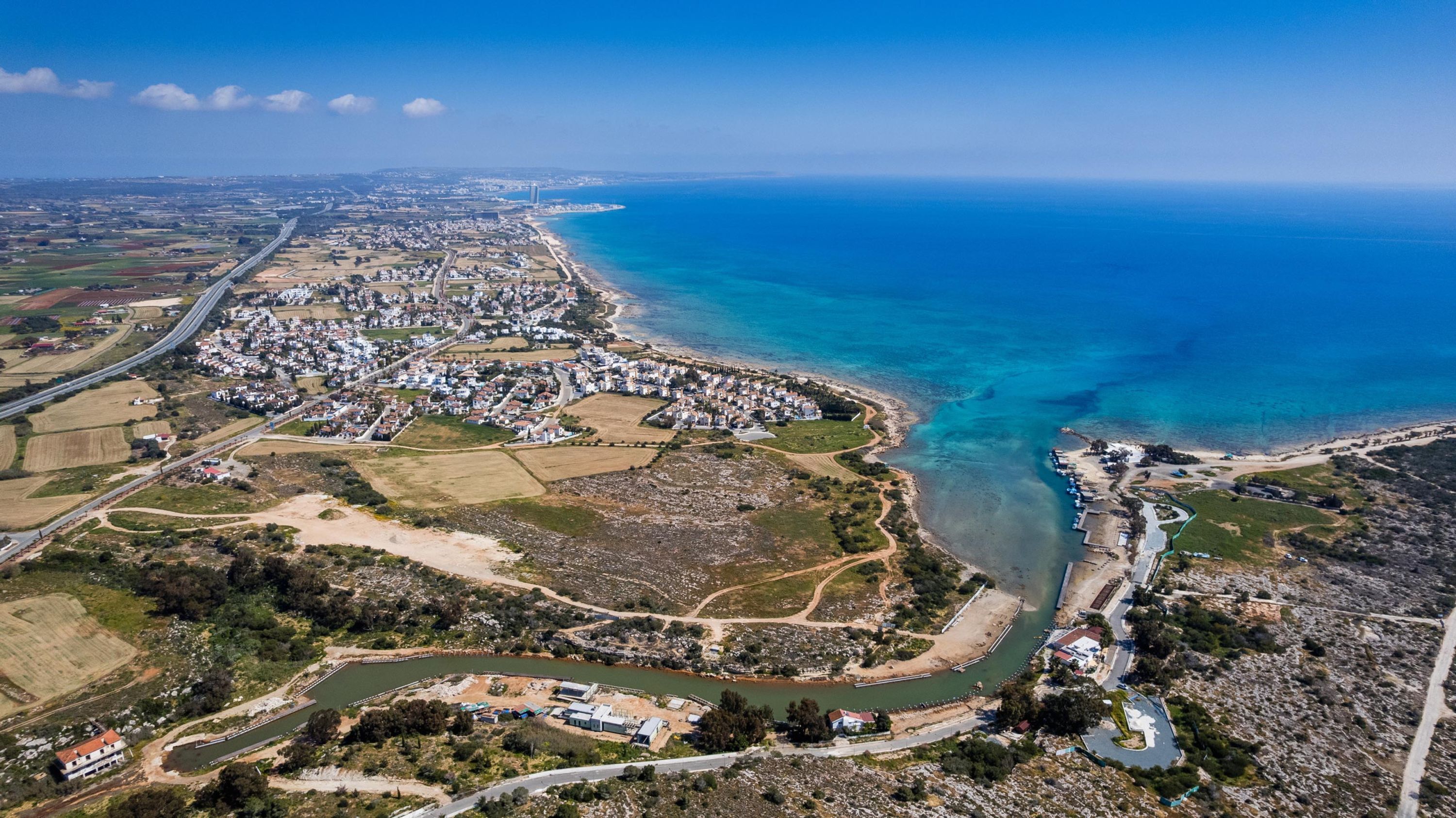 Une vue aérienne d’une ville côtière, avec un ensemble dense de bâtiments le long du littoral, une rivière serpentant à travers le centre et une mer bleue et limpide.