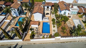 Eine Vogelperspektive zeigt ein Wohnhaus mit zwei Swimmingpools, einer Terrasse und einem kleinen Garten.