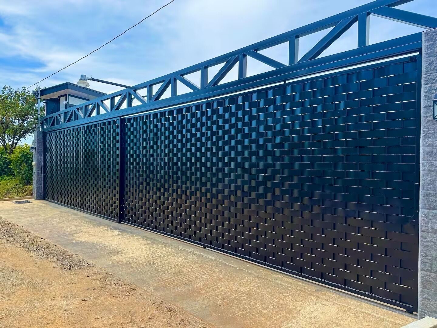 A modern metal fence with a geometric pattern, a concrete pathway, and a building with a stone facade in the background.