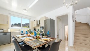A modern kitchen with a dining area, a staircase, and a view of the outdoors. - Green Bay Villa 16 in Protaras (Paralimni)