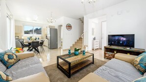 A modern living room with a sofa set, a coffee table, a TV, and a staircase leading to another level. - Green Bay Villa 16 in Protaras (Paralimni)