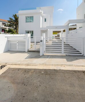 A modern building with a white exterior, a gated entrance, and a staircase leading to the upper levels. - Green Bay Villa 16 in Protaras (Paralimni)