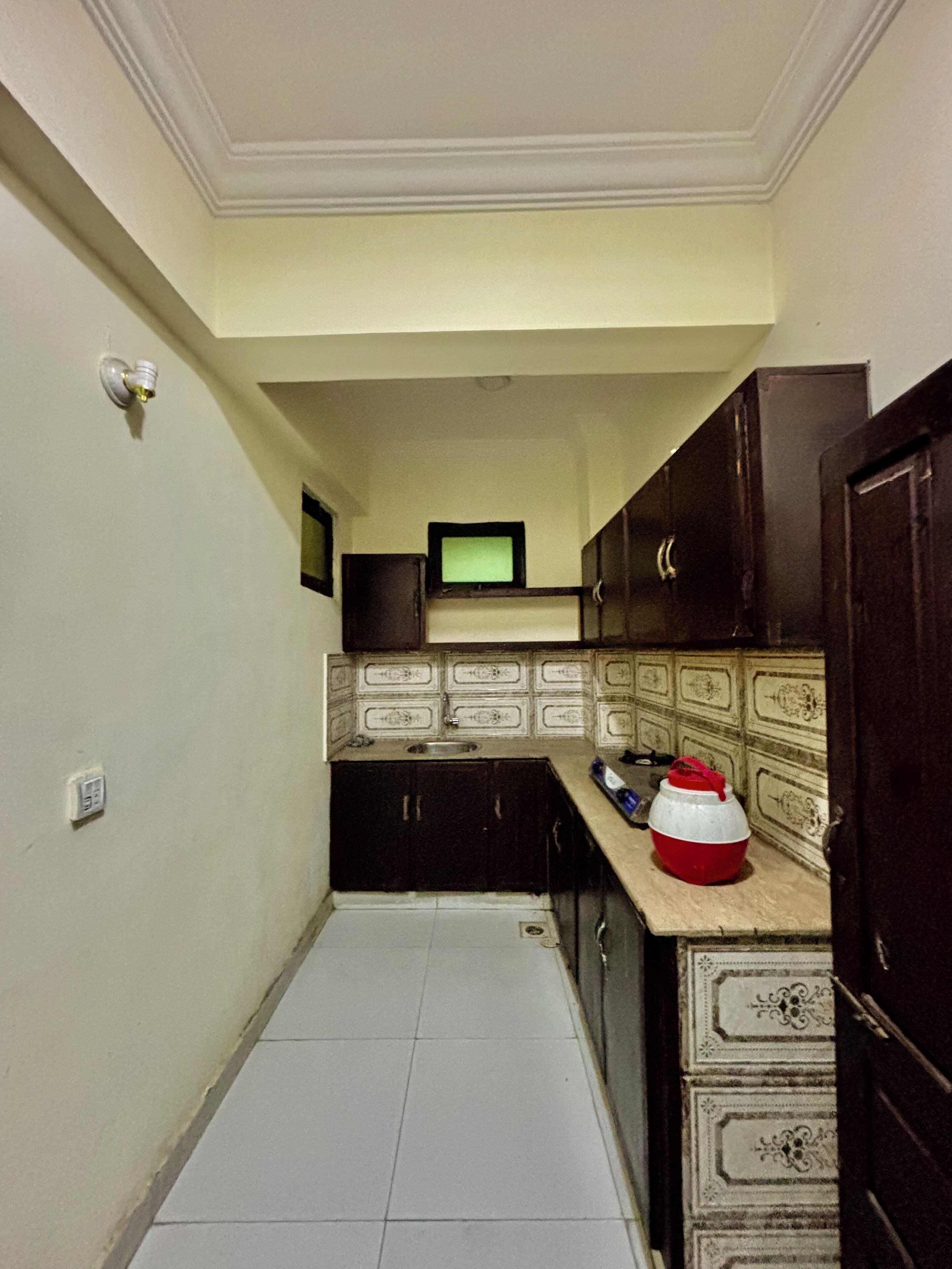 Una cocina estrecha con armarios oscuros, salpicadero de azulejos y un televisor pequeño en la pared.
