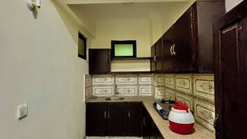 Una cocina estrecha con armarios oscuros, salpicadero de azulejos y un televisor pequeño en la pared.