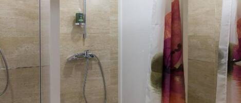 A glass-enclosed shower with a handheld showerhead and a wall-mounted faucet.