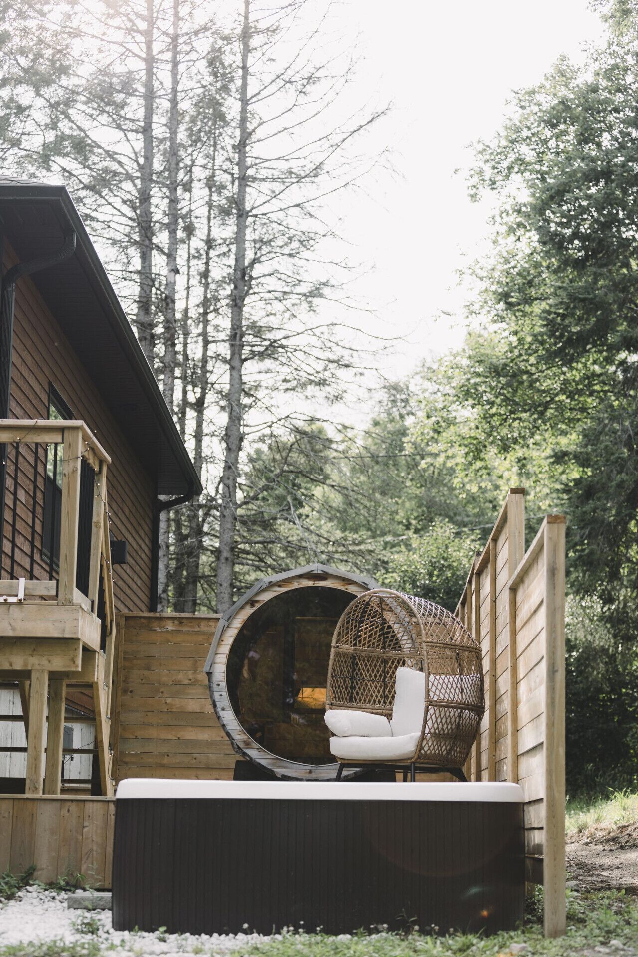 Une cabane en bois avec un bain à remous, un fauteuil en osier et une fenêtre ronde.