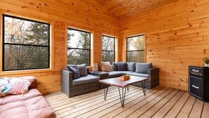 A cozy cabin interior with a wooden interior, large windows, a sofa, a table, and a speaker. - All Season Muskoka Cottage*HotTub*Sauna*Beach*BBQ (Huntsville)