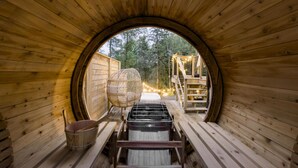 A wooden sauna with a circular opening, a wicker chair, a wooden bench, and a sauna heater. - All Season Muskoka Cottage*HotTub*Sauna*Beach*BBQ (Huntsville)
