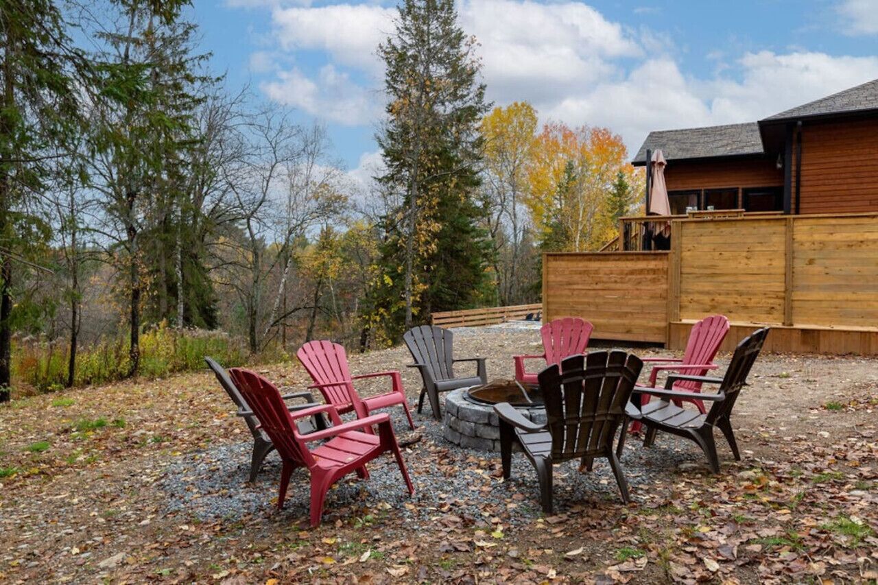 A wooden cabin with a fire pit and Adirondack chairs in a forest setting.