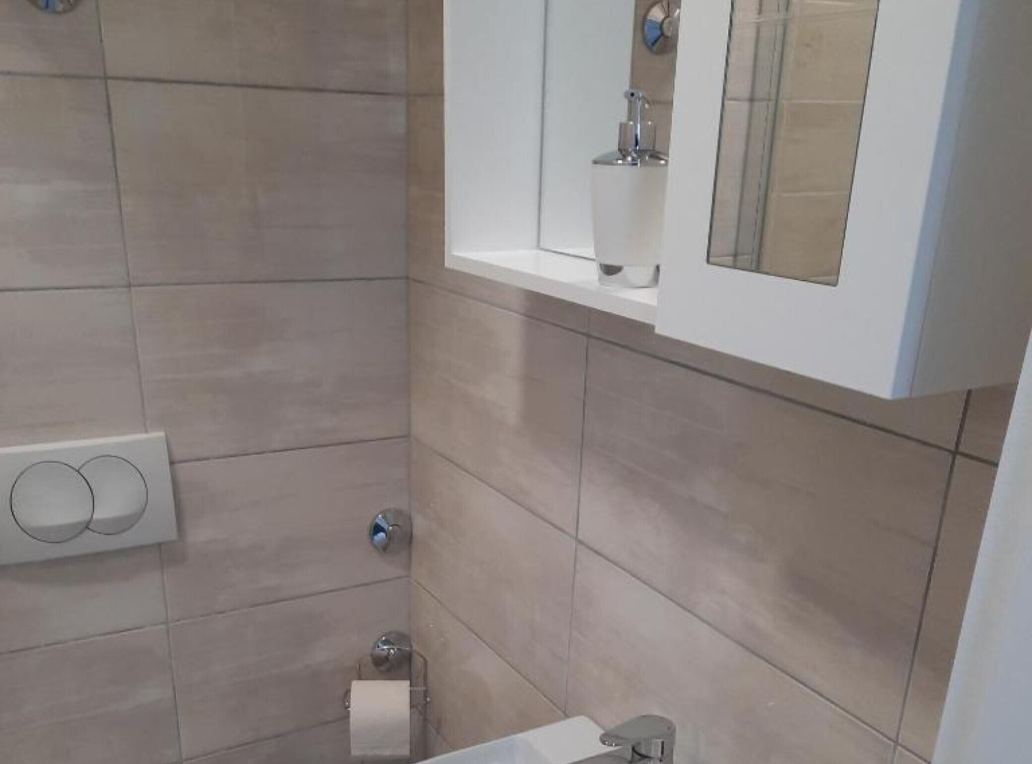Une salle de bain avec des carreaux de couleur beige, un lavabo blanc, un miroir et des toilettes.