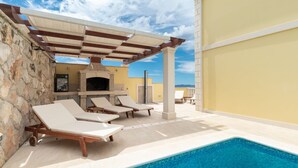 A poolside area with lounge chairs, a stone wall, a tiled pool, and a pergola.