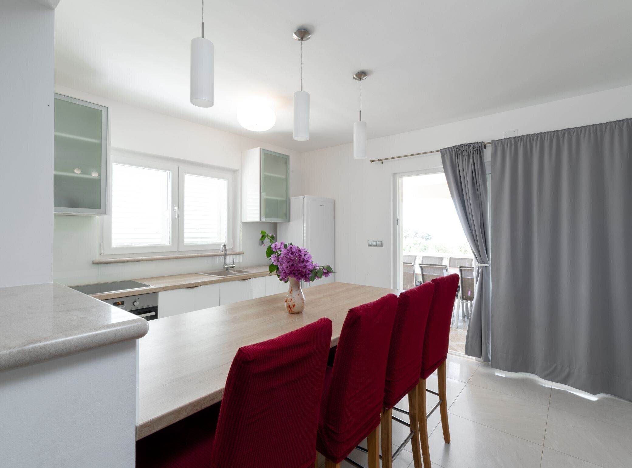 Eine moderne Küche mit Essbereich, ausgestattet mit einem Holztisch, roten Stühlen und Pendelleuchten.