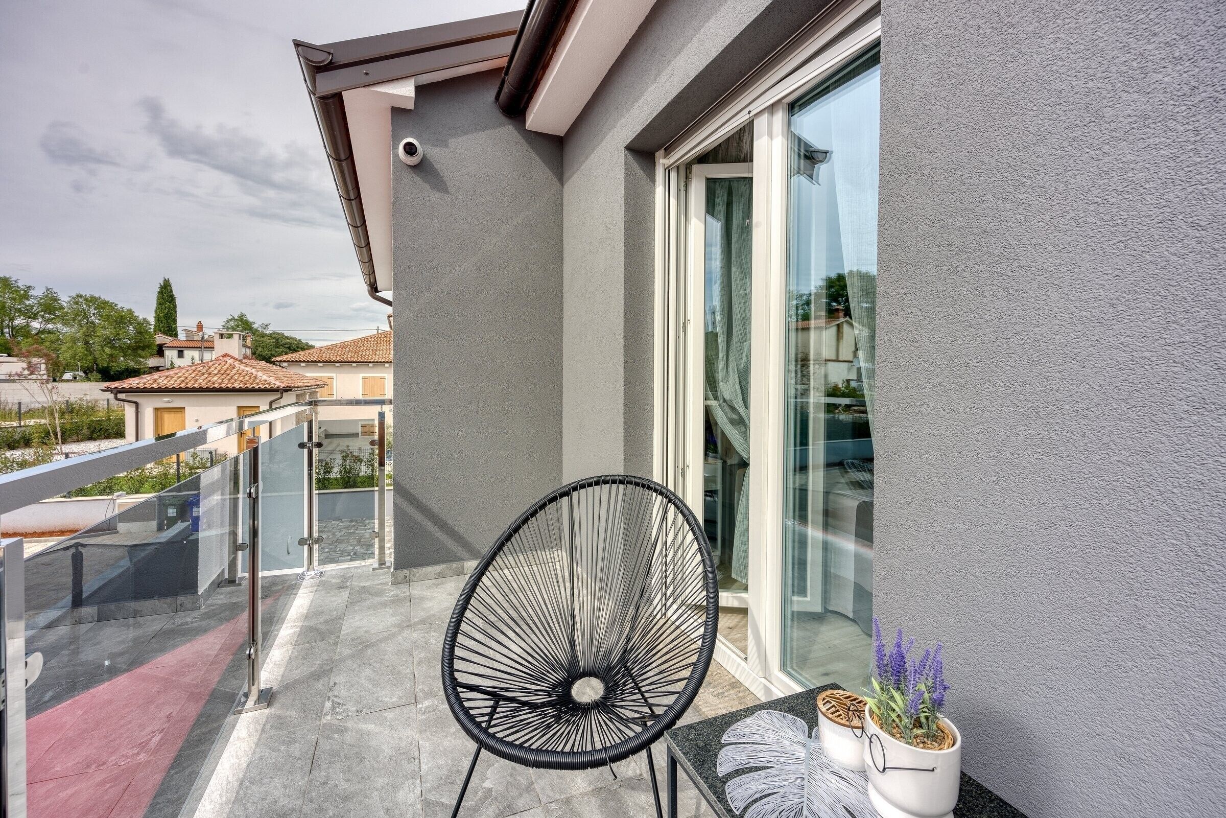 A balcony with a glass door, a black chair, and two potted plants.