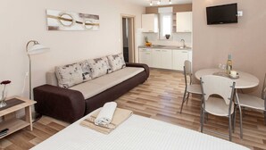 A modern hotel room with a sofa, a bed, a small table with a bottle and glasses, a TV, and a kitchenette in the background. - Beachfront Apartments for Relaxing Getaways in Crikvenica - Junior Studio Apartment 2 2 (Crikvenica)