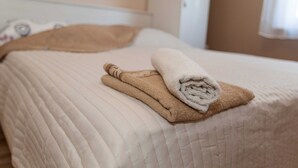 Una cama bien hecha con un edredón color beige y dos toallas enrolladas.