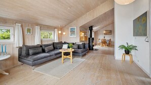 Una sala de estar moderna con un sofá gris, piso de madera, una mesa redonda de madera y un estufa de leña negra.