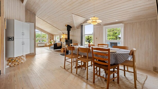 Un comedor espacioso con techo alto y vigas de madera, una mesa central con sillas, y vistas al exterior a través de amplios ventanales.