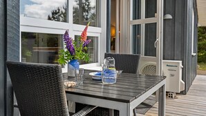 Un patio al aire libre con una mesa, sillas, una jarrón de agua y un florero con flores.
