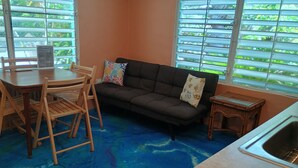 A living room with a sofa, two chairs, a small table, and a kitchen area with a sink.