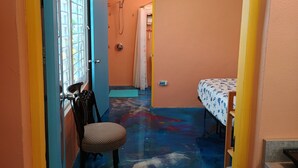 A narrow hallway with a chair, a bed with a patterned bedspread, and an air conditioning unit mounted on the wall.