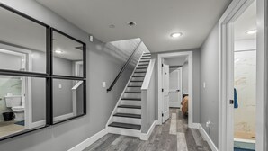 A modern home interior with a staircase leading to a second floor, a hallway with a mirror, and a bathroom with a shower. - Serenity Stays Charming 3bd 2.5ba Oasis (Philadelphia)
