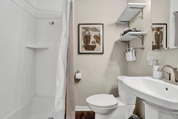 A bathroom with a toilet, sink, and shower area. There are framed leaf artworks on the wall.