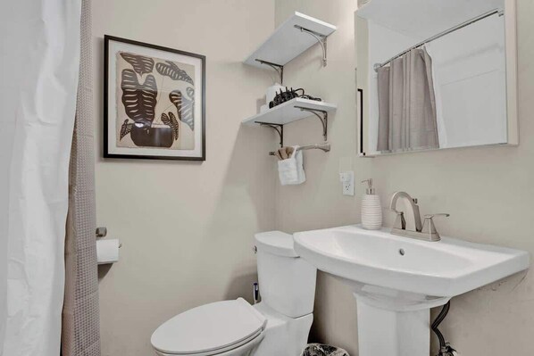 Een badkamer met toilet, wastafel en een kunstwerk in een lijst aan de muur.