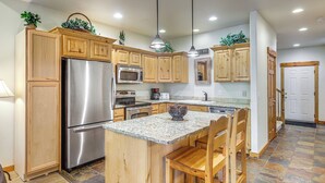 A kitchen with wooden cabinets, stainless steel appliances, a granite countertop, and a central island with chairs. - 1 Mi to Ponderosa State Park: Condo w/ Pool Access (McCall)