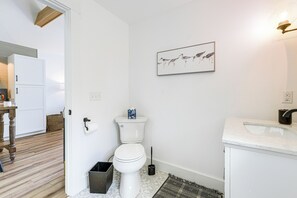 Une salle de bain avec des toilettes, un lavabo et une œuvre d’art représentant un oiseau, encadrée et accrochée au mur.