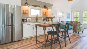 Een moderne keuken met een roestvrijstalen koelkast, een houten tafel en barstoelen. Er is een raam dat natuurlijk licht en uitzicht op de omgeving biedt.