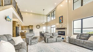 Uma sala de estar espaçosa com um amplo sofá modular cinzento, uma poltrona cinzenta menor e um banquinho combinando. É visível, ao fundo, uma área de jantar com uma mesa e cadeiras de madeira.