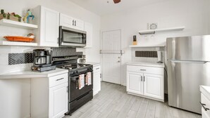 Una cocina moderna con armarios blancos, un refrigerador de acero inoxidable, un microondas, una estufa y un ventilador de techo.