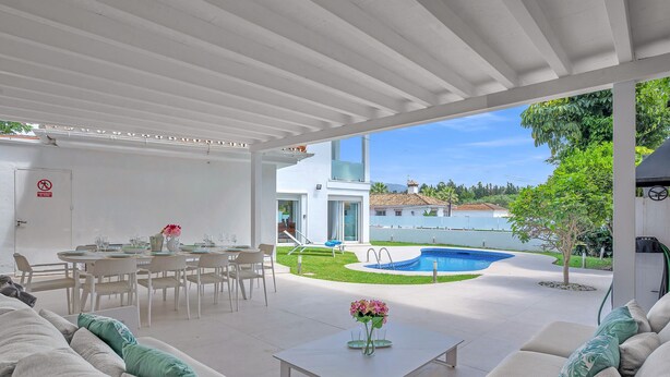 A covered outdoor area with a pool, dining setup, and seating. - Villa Banus (Marbella)