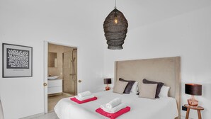 A hotel room with a large bed, two bedside tables with lamps, a modern pendant light, a framed artwork on the wall, and a bathroom visible through an open door. - Villa Banus (Marbella)