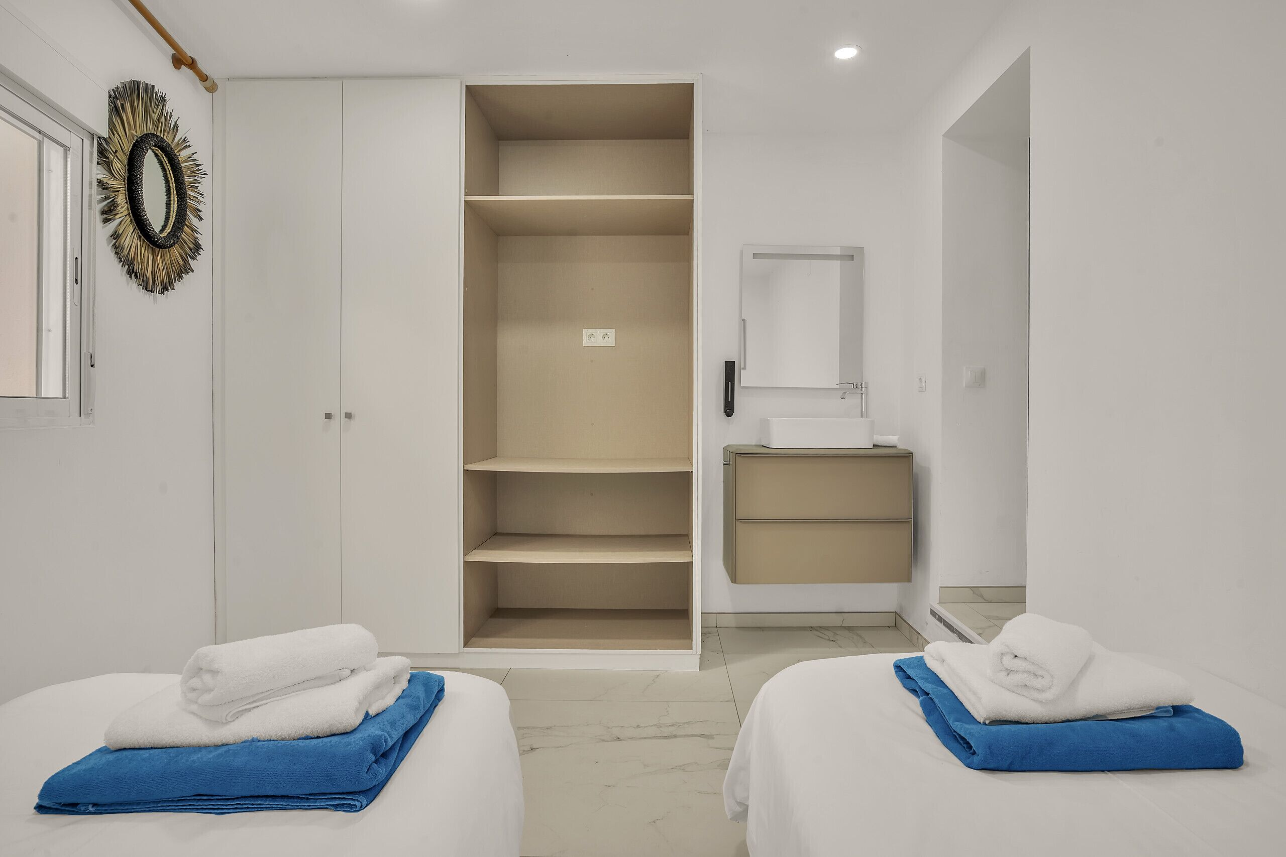 A hotel room with two beds, a wardrobe, a mirror, and a sink.