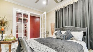 A bedroom with a bed, a nightstand, a lamp, a vase with a plant, and a closet with a red door. - Golf, Fish & More: Cozy ‘Safari Unit’ in Atwater! (Atwater)